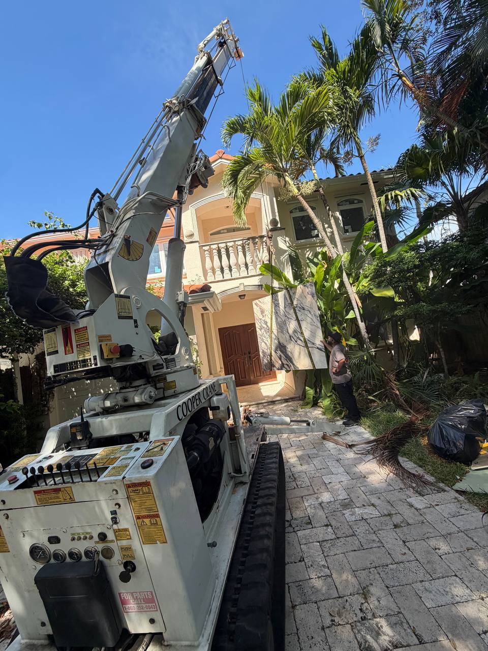 Cooper Crane mini spider crane set up on a paver driveway beside a house